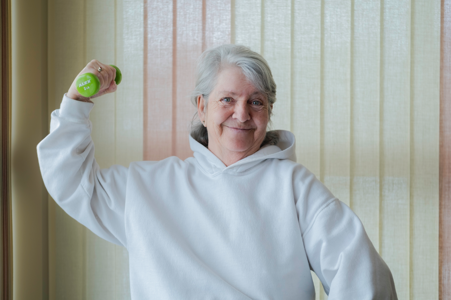 Smiling senior woman in a white hoodie lifting a green dumbbell. Smiling senior woman in a white hoodie lifting a green dumbbell.