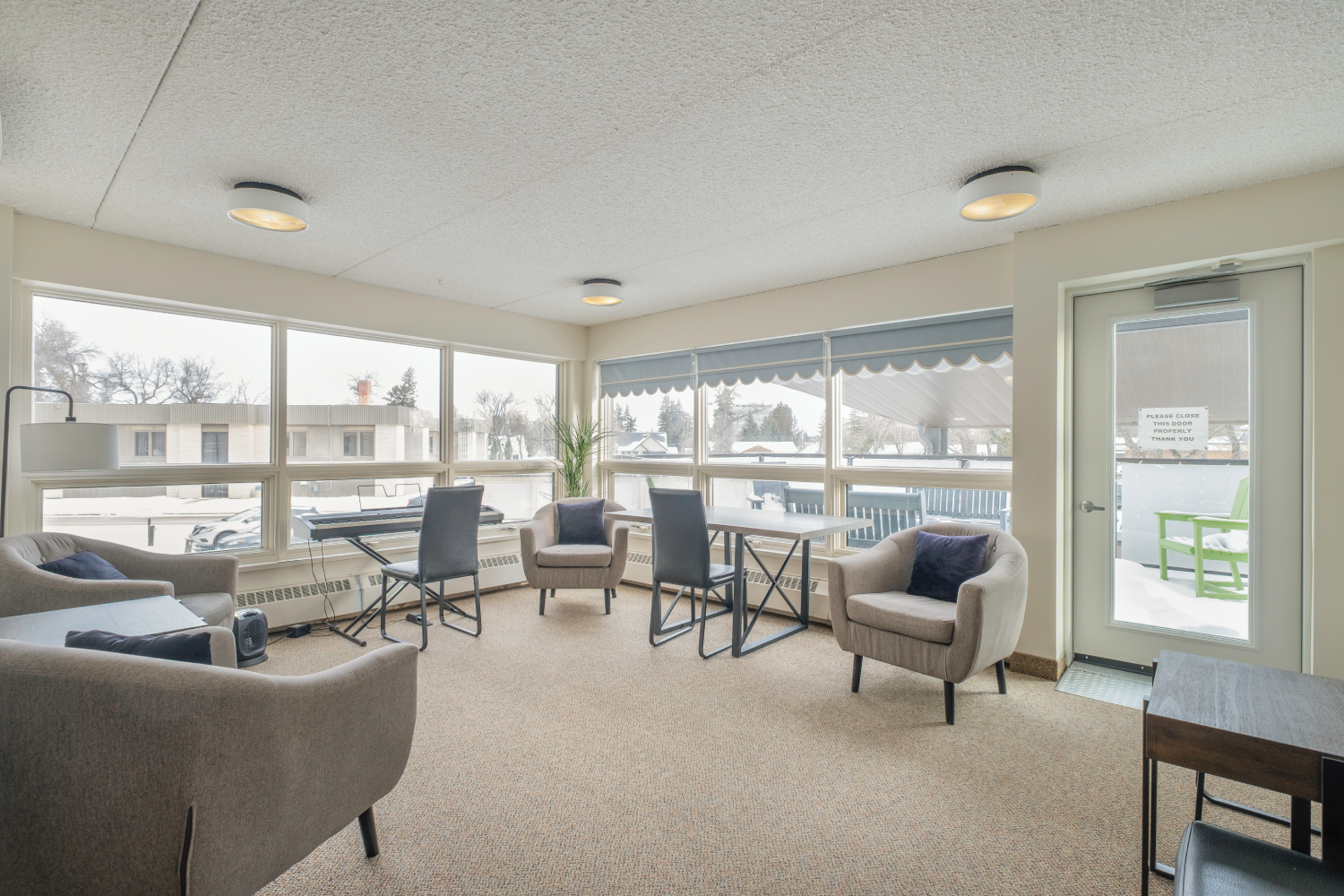 Well-lit room with large windows, comfortable seating, a small table, and a keyboard, creating a cozy space for relaxation or socializing. Well-lit room with large windows, comfortable seating, a small table, and a keyboard, creating a cozy space for relaxation or socializing.
