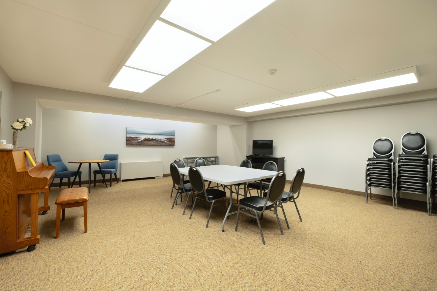 Well-lit room with large windows, comfortable seating, a small table, and a keyboard, creating a cozy space for relaxation or socializing.