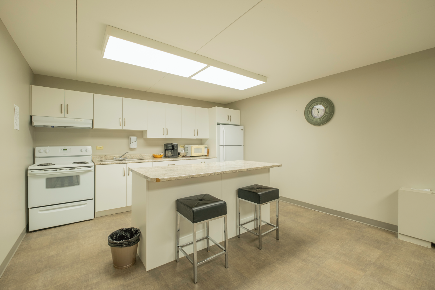 Well-lit, modern kitchen with white cabinets, granite countertop island, and two black bar stools.